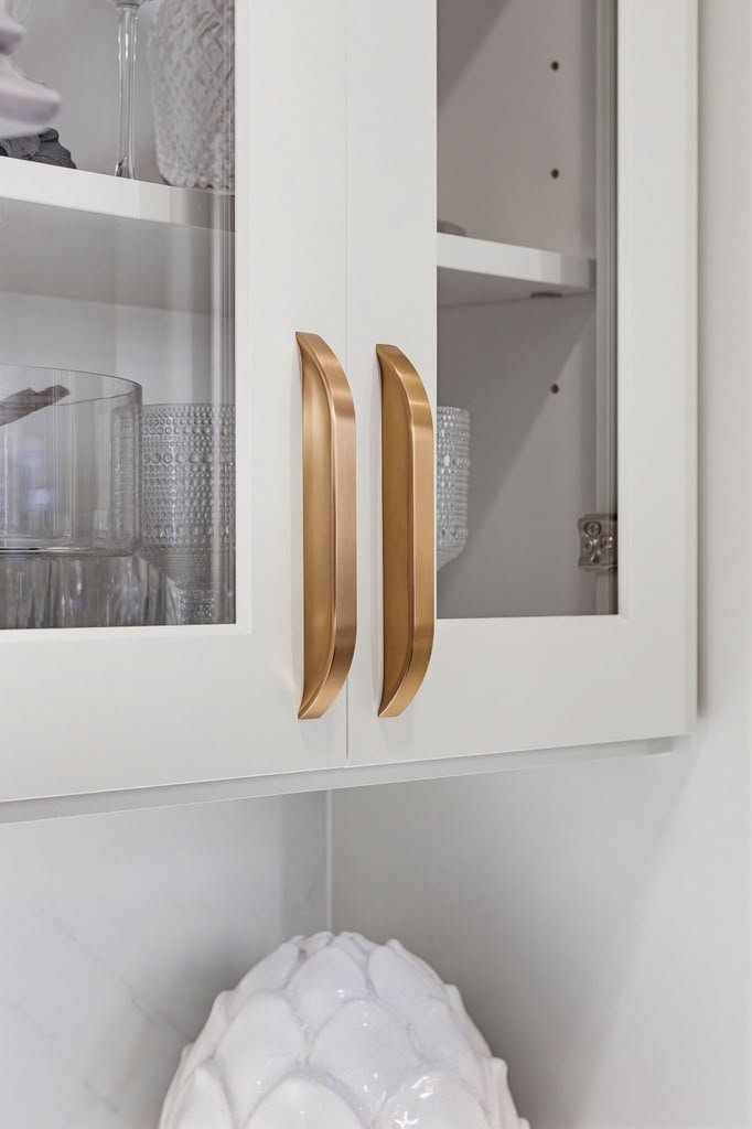 Brass pulls on white glass-front cabinetry