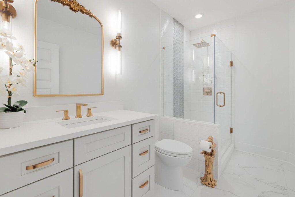 Guest bathroom after the redesign, with a white shaker vanity, brass fittings and a gilt arched mirror
