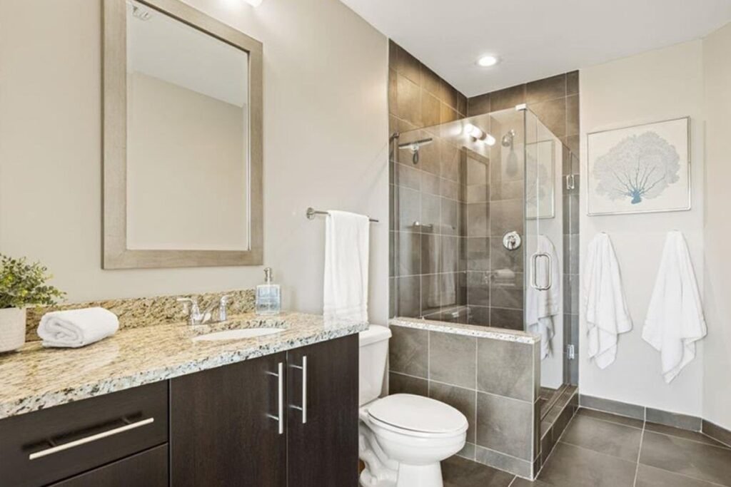 Guest bathroom before the redesign, with espresso cabinets, a granite counter and a grey tile shower
