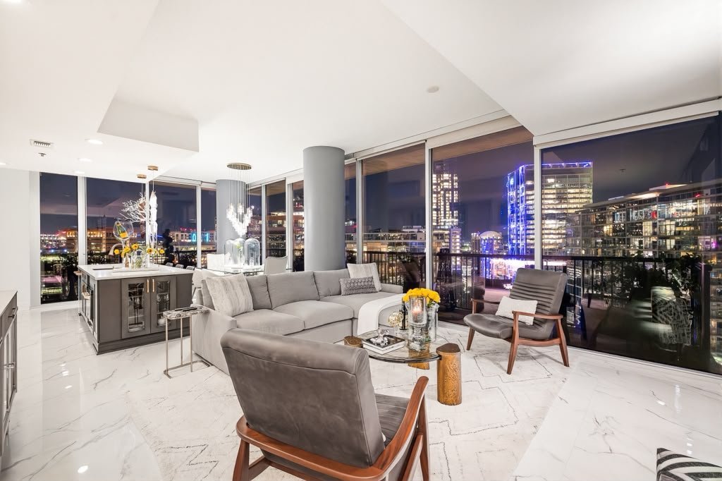 Living room with white marble floors, a grey sectional and city views at night