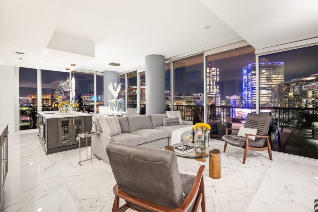 Penthouse living room after the redesign, with white marble floors, a grey sectional and the city lit up at night