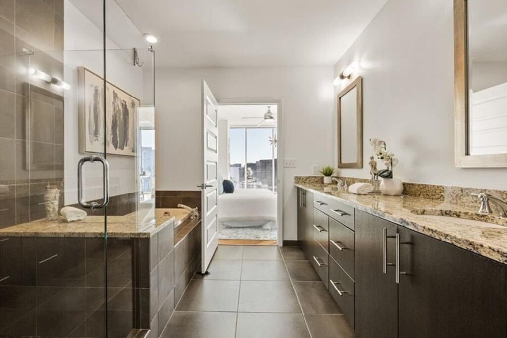 Primary bathroom before the redesign, with granite counters, brown tile and a built-in tub