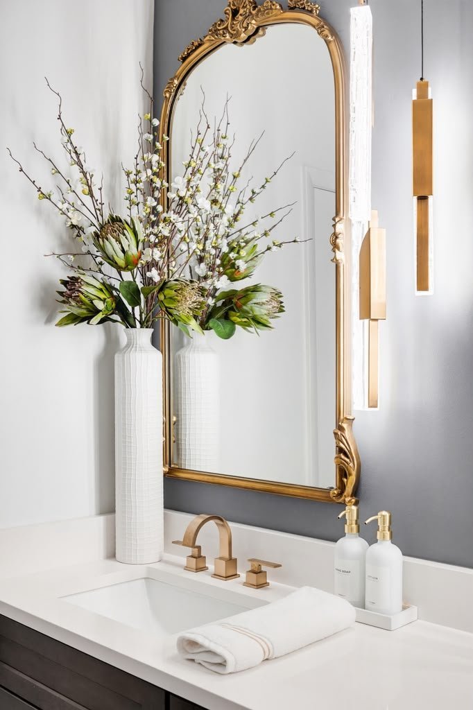 Powder room with a gold arched mirror on a charcoal wall